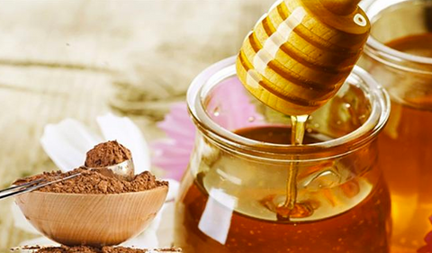 Honey dripping from a wooden dipper into a jar beside a bowl of ground cinnamon