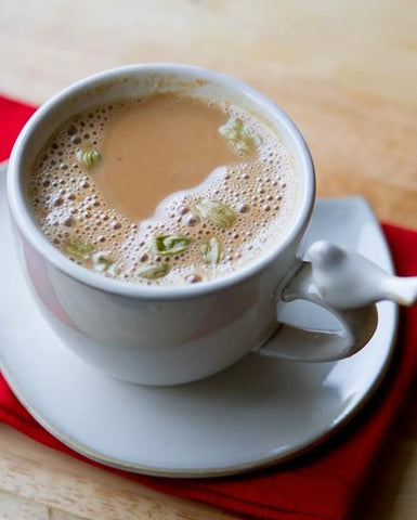 Cup of milky coffee with floating cardamom pods on a saucer and red napkin