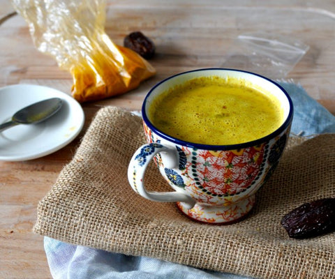 Patterned mug of golden spiced milk on a burlap cloth beside dates