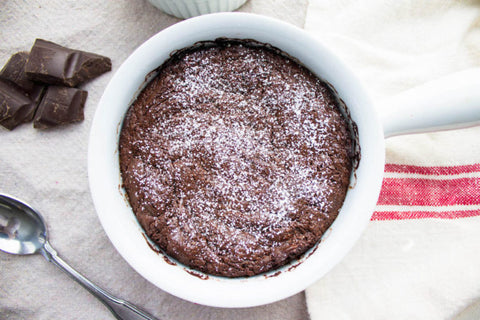 Chocolate cake in a white ramekin dusted with powdered sugar, chocolate pieces beside it