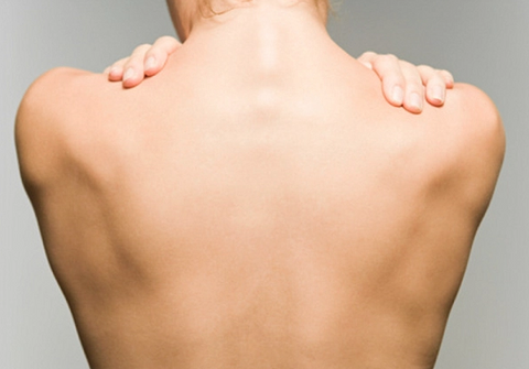 Bare upper back of a person with both hands resting on their shoulders