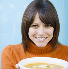 Smiling woman in an orange sweater holding a bowl of soup