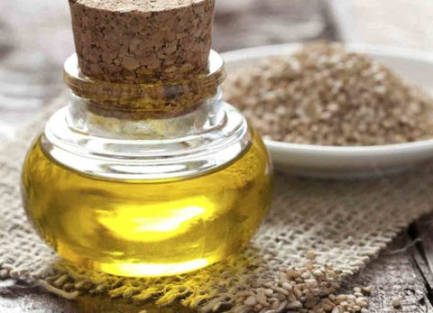Corked glass bottle of sesame oil with a bowl of sesame seeds on burlap