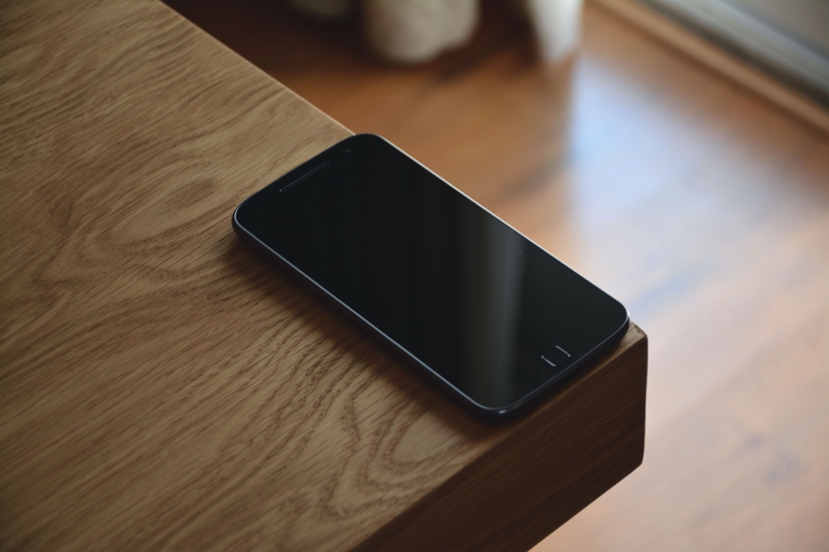 A smartphone with a dark screen resting on the corner of a wooden table