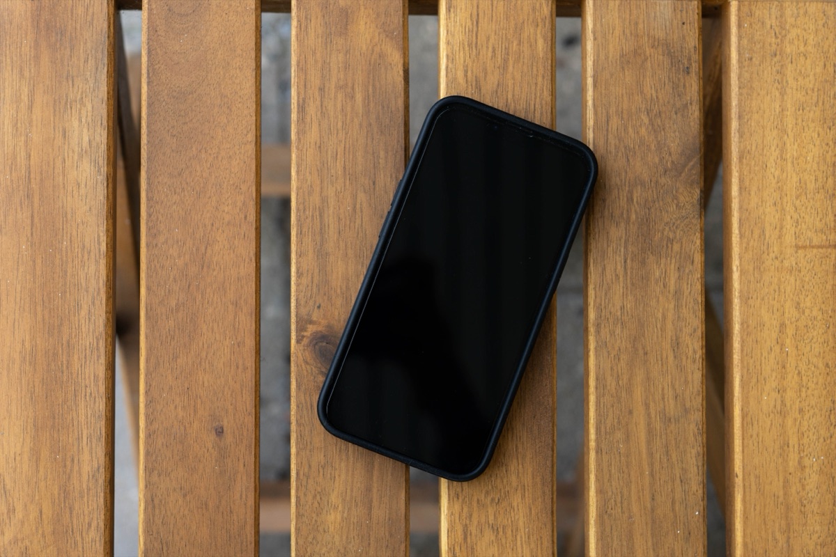 A smartphone with a black screen lying on a slatted wooden table, seen from above