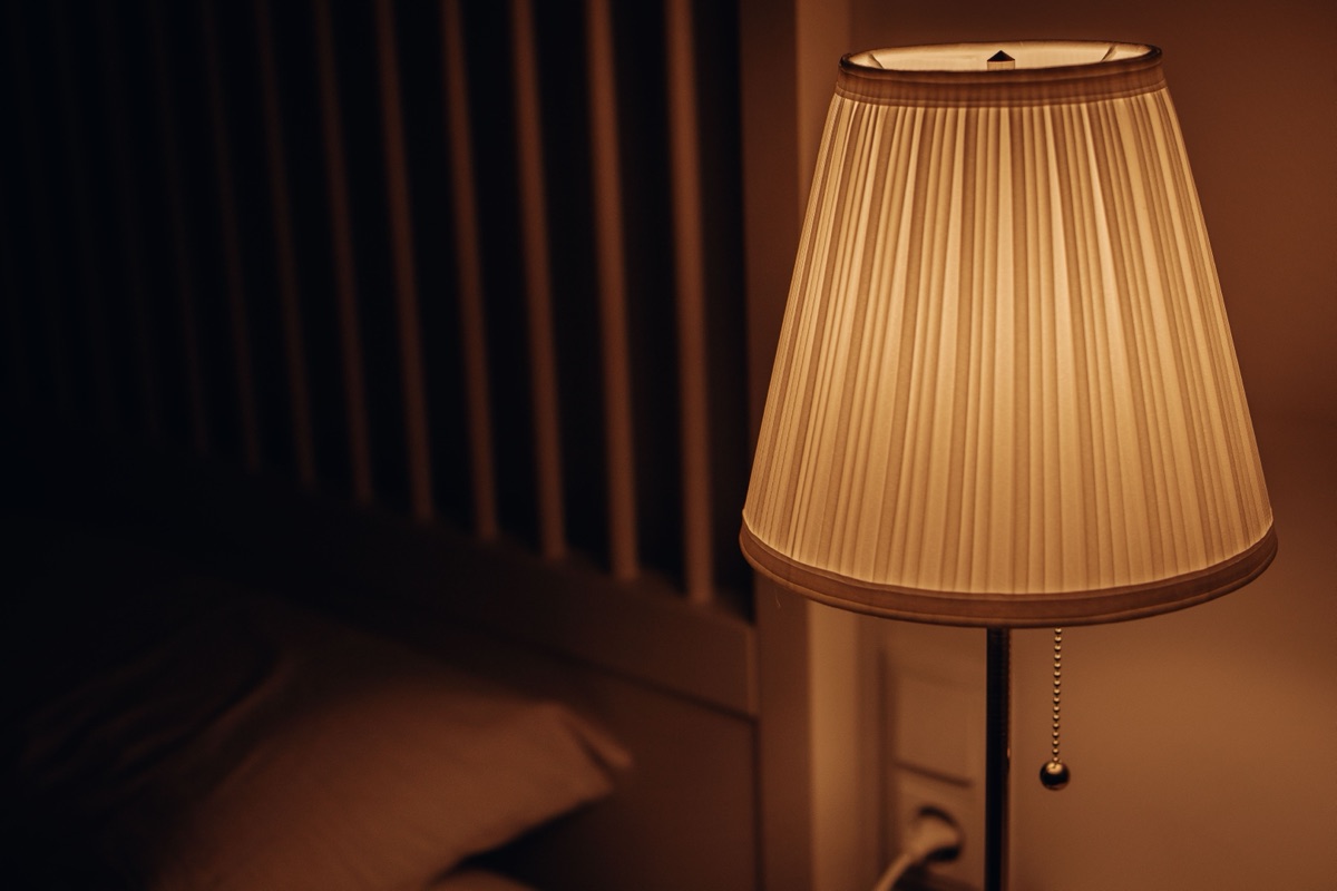 A pleated lampshade glowing softly beside a pillow in a dark bedroom