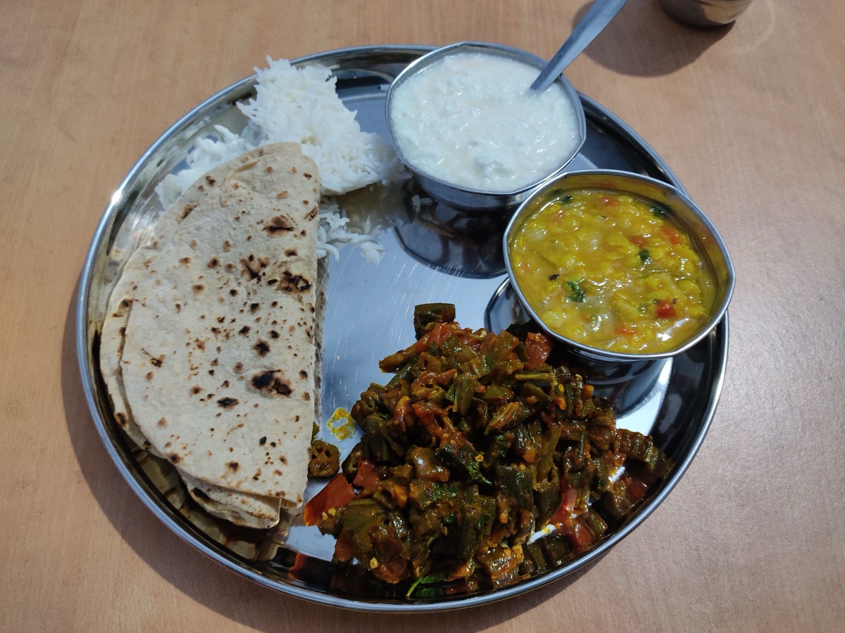 A steel plate with chapati, rice, yellow dal, cooked okra and a small bowl of yogurt