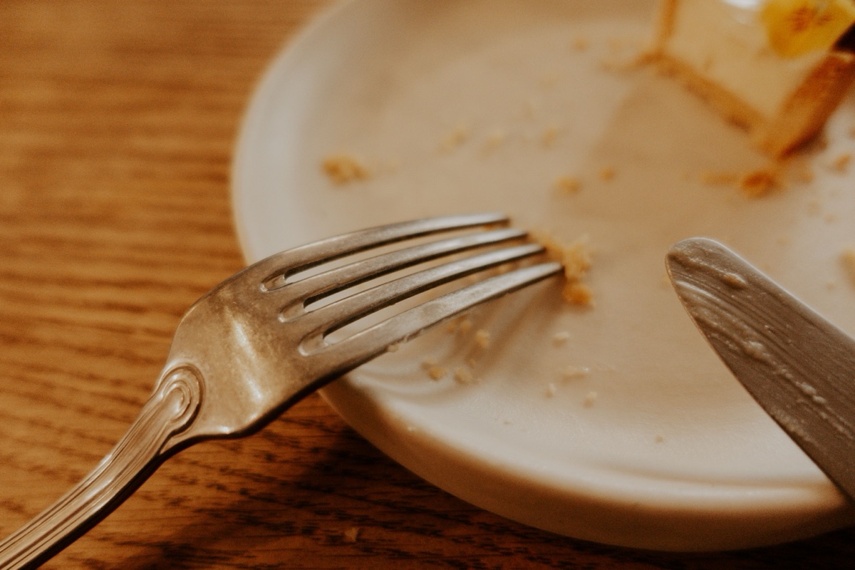 A fork and knife on a white plate of crumbs and a last bite of cake, on a wooden table