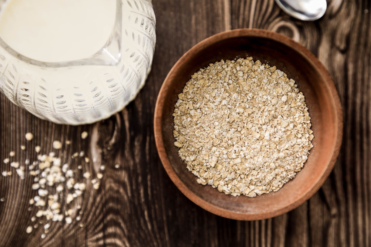 Wooden bowl of oats beside a glass jug of milk on a dark wooden table