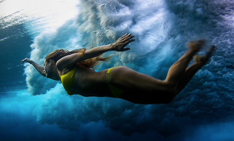 Woman in a yellow bikini diving underwater beneath a breaking ocean wave