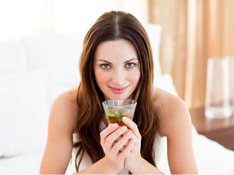 Smiling woman with long brown hair holding a glass of herbal tea with mint leaves