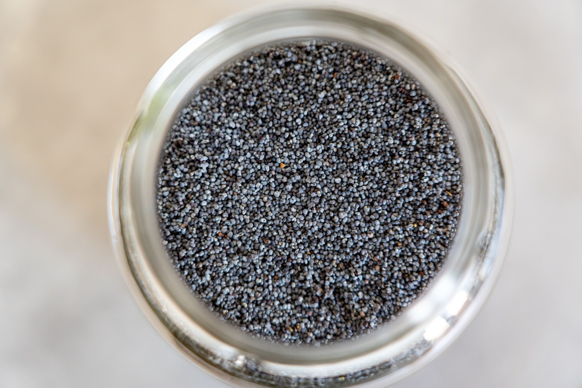 Top-down view of dark blue-grey poppy seeds filling a clear glass jar on a pale surface