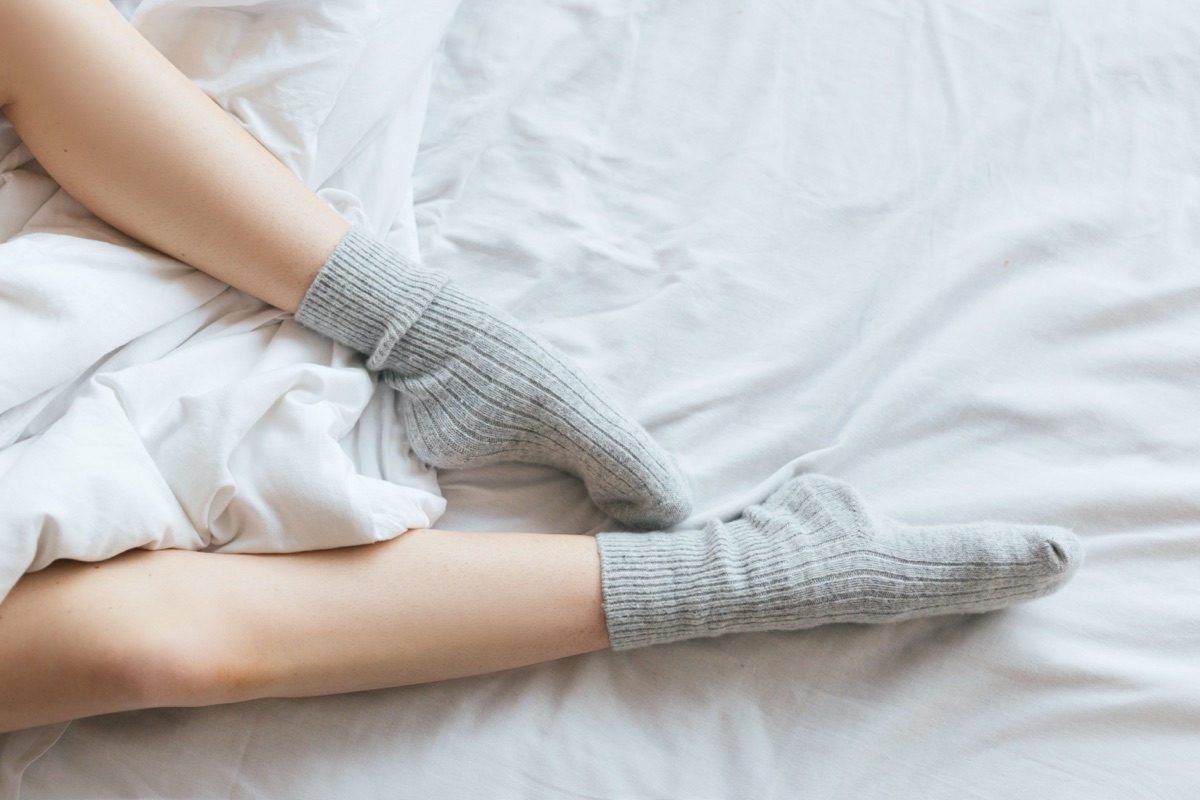 Feet in grey ribbed knit socks resting on rumpled white bed sheets