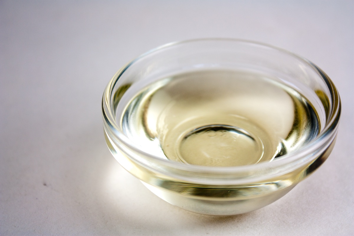 A small clear glass bowl holding a shallow pool of pale yellow oil on a white surface