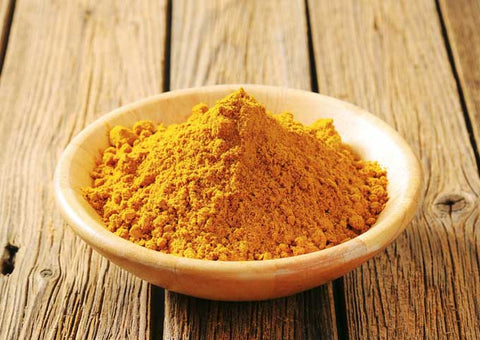 Wooden bowl of yellow curry powder on a rustic wooden table