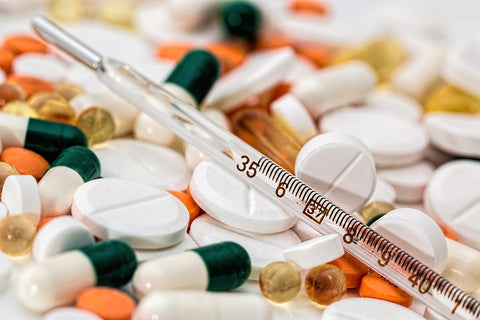 Glass thermometer lying on a pile of assorted white tablets and colored capsules