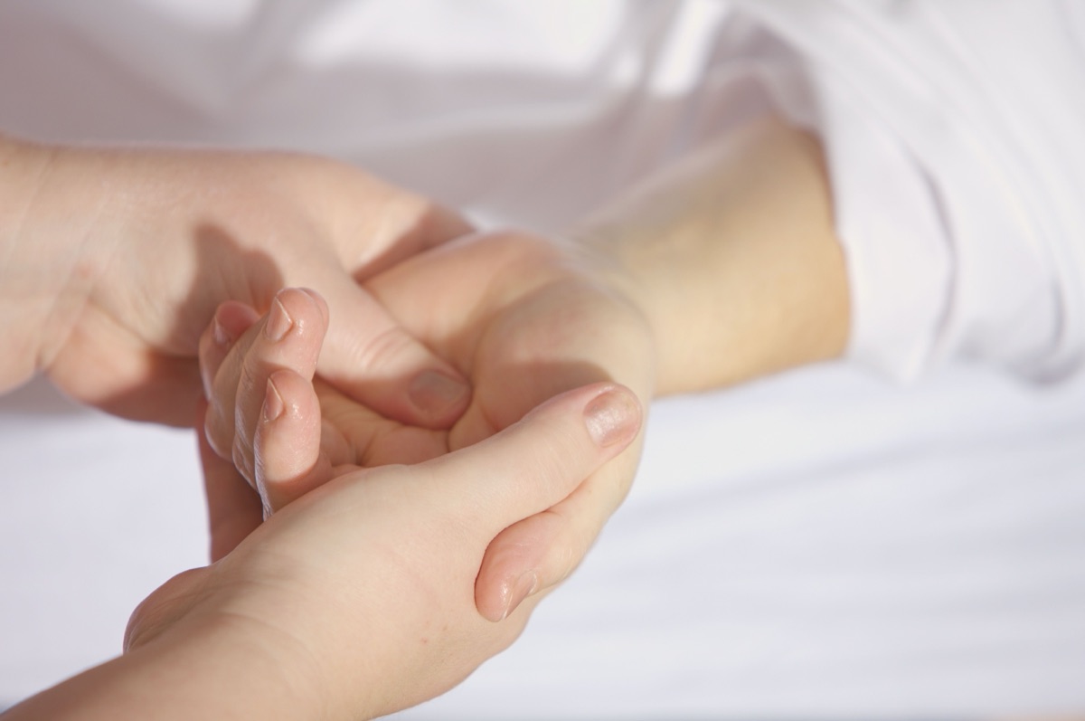 Close-up of one person pressing a thumb into the centre of another person’s open palm, against white fabric