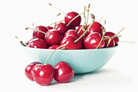 Light blue bowl filled with fresh red cherries on stems, with a few cherries in front