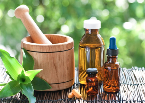 Wooden mortar and pestle with amber bottles of herbal oil and a dropper bottle beside a green plant