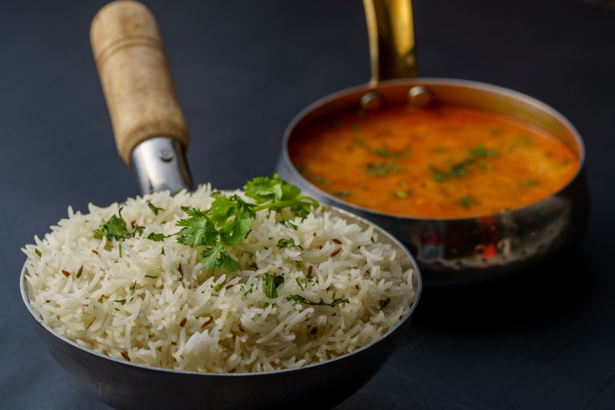A small pan of cumin rice topped with coriander beside a pan of dal on a dark table