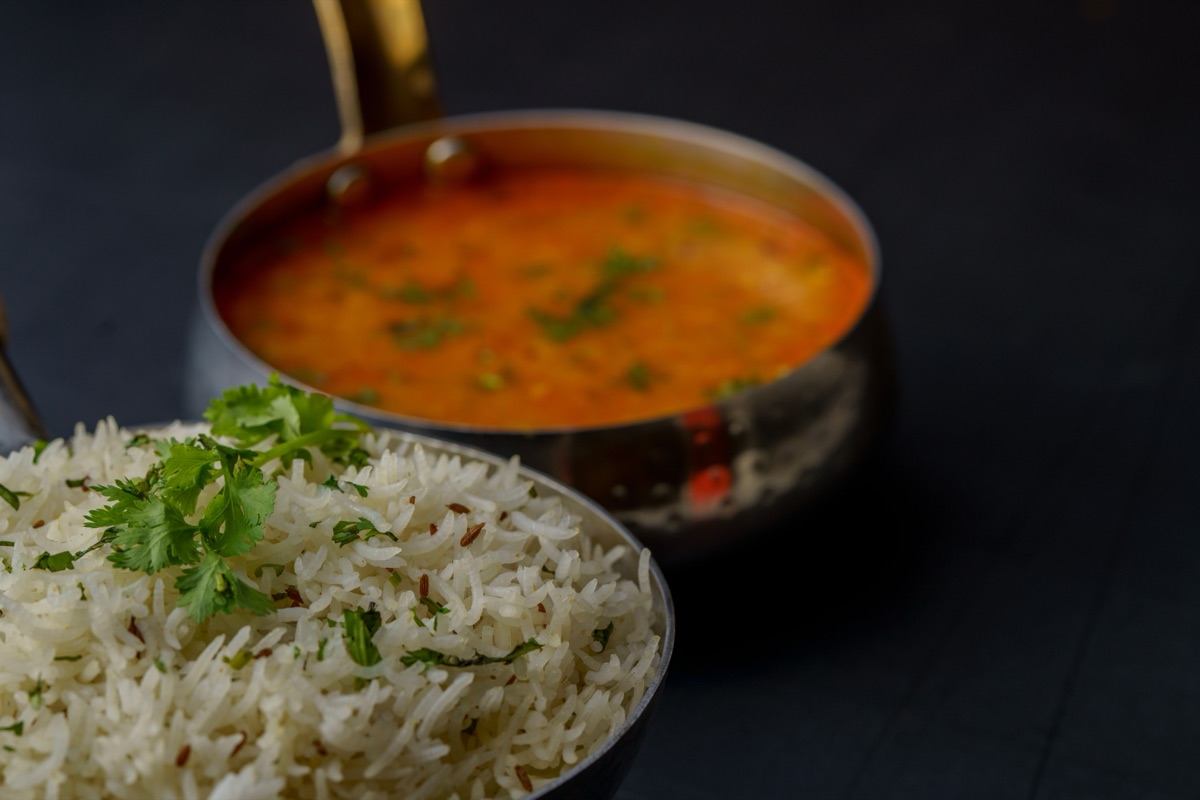 A metal pan of orange-yellow dal next to a bowl of cumin rice topped with fresh cilantro