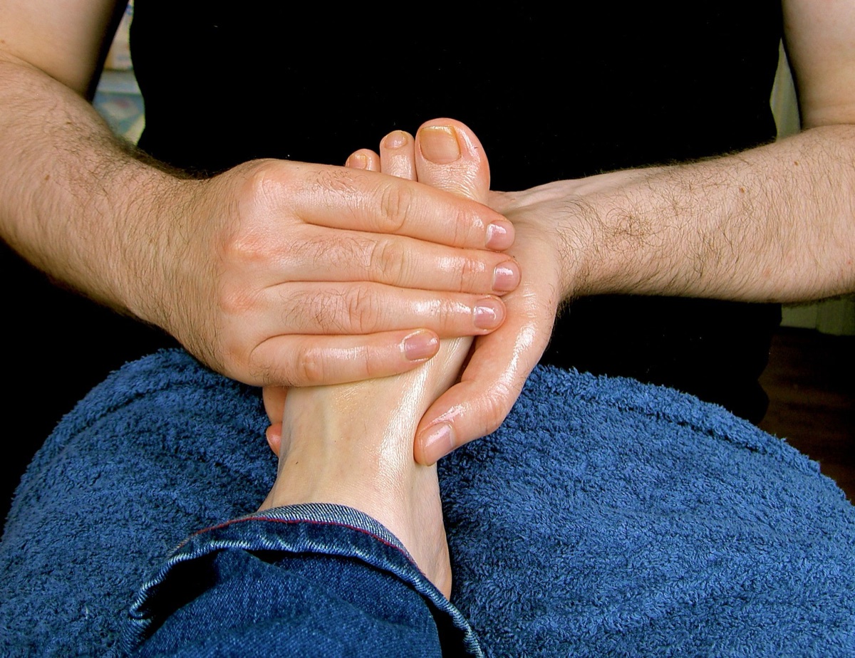Two oiled hands wrapped around the top of a bare foot and its toes, the foot resting on a blue towel