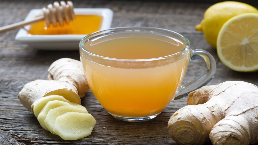 Glass cup of ginger tea with sliced fresh ginger root, honey and a halved lemon