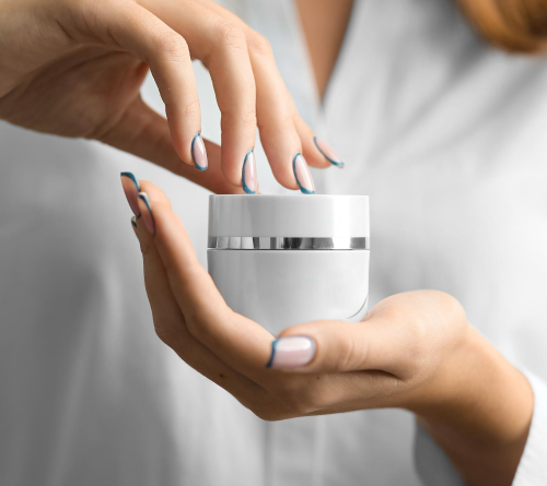 Hands with manicured nails opening a white jar of skin cream