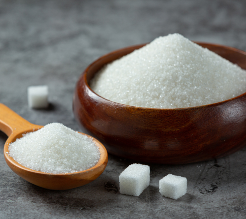 Granulated sugar in a wooden bowl and wooden spoon with sugar cubes on a gray surface