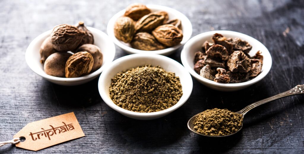 Three bowls of dried fruits and a bowl of Triphala powder, with a tag reading triphala
