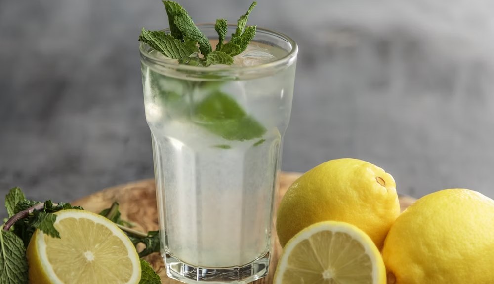 Glass of lemon water with fresh mint leaves beside halved lemons