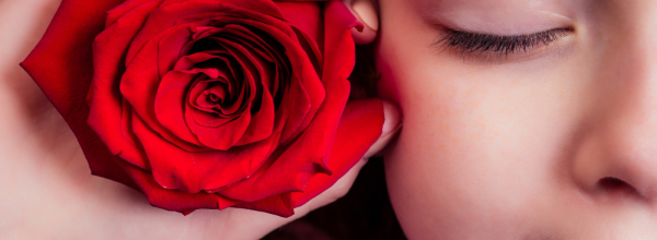 Hand holding a red rose against a woman's cheek, her eyes closed