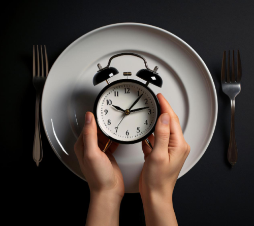 Hands holding an alarm clock over an empty white plate set between two forks