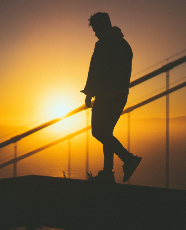 Silhouette of a man walking along a railing at sunrise with the sun low behind him