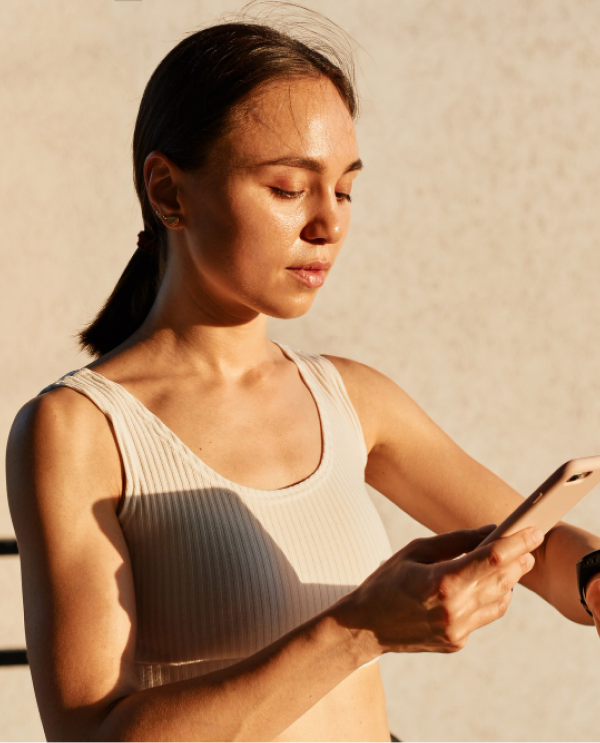 Woman in a ribbed sports top looking at her phone in warm sunlight