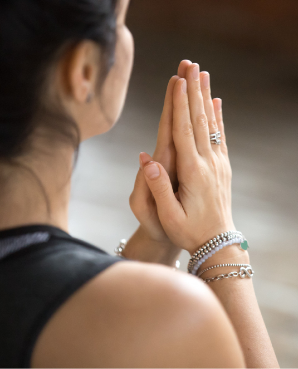 Woman seen from behind with palms pressed together in prayer position, wearing silver bracelets