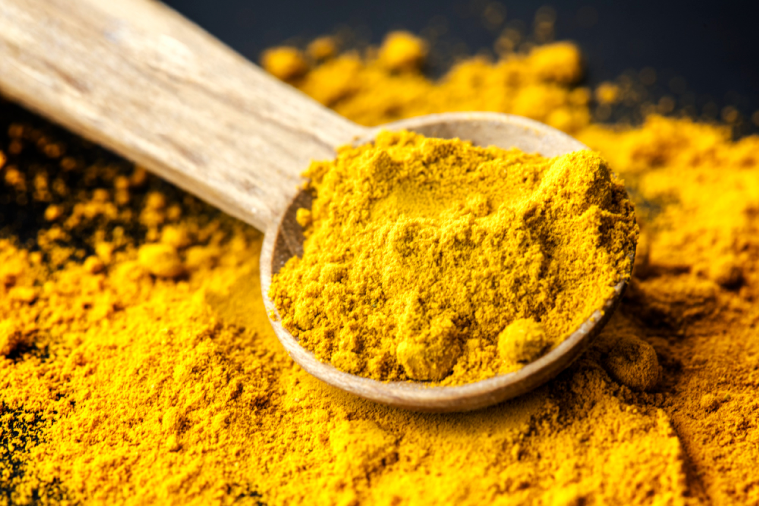 Wooden spoon heaped with bright yellow turmeric powder on a bed of spilled turmeric