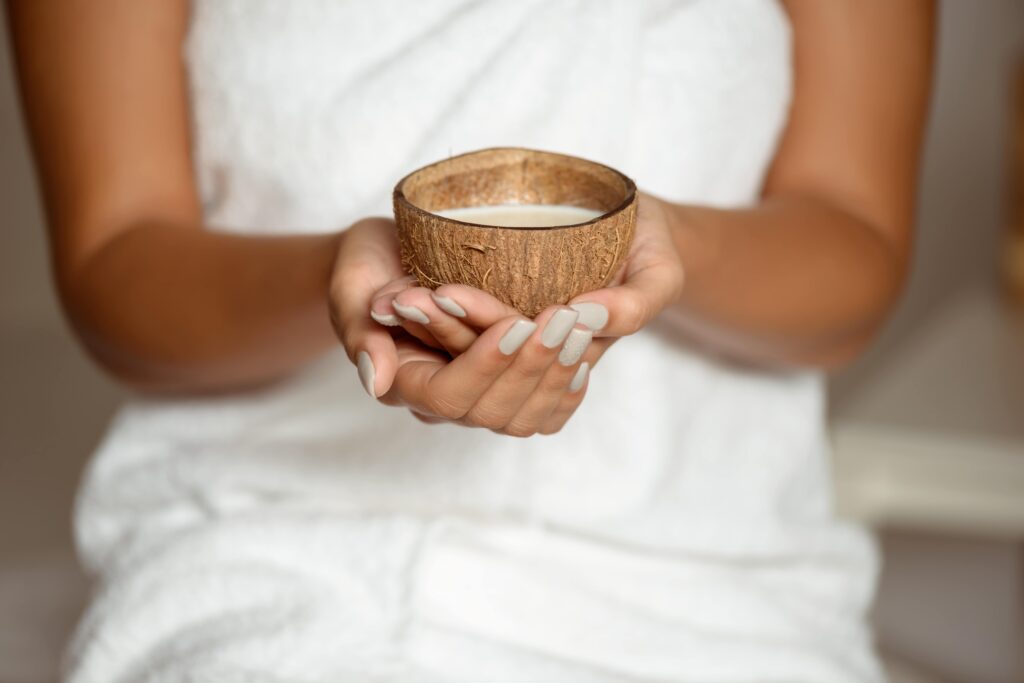 Hands holding a coconut shell cup filled with milky liquid, with a white towel behind