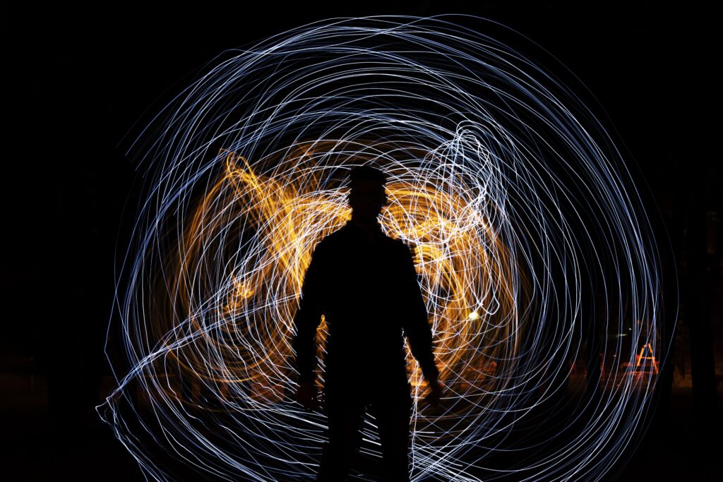 Silhouette of a man standing in front of swirling blue and orange light trails at night