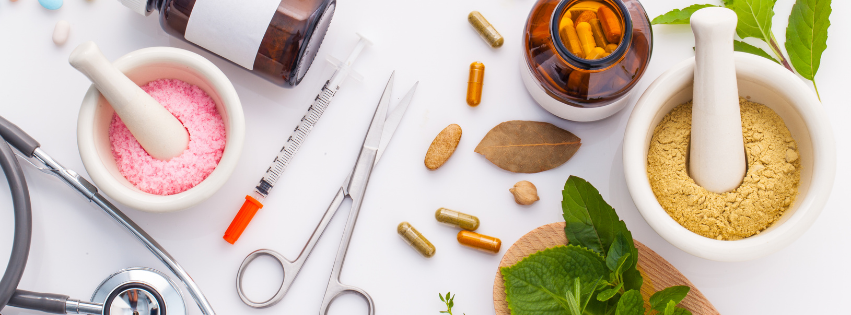 Mortars of pink salt and herbal powder beside capsules, a bay leaf, mint, a syringe, scissors and a stethoscope